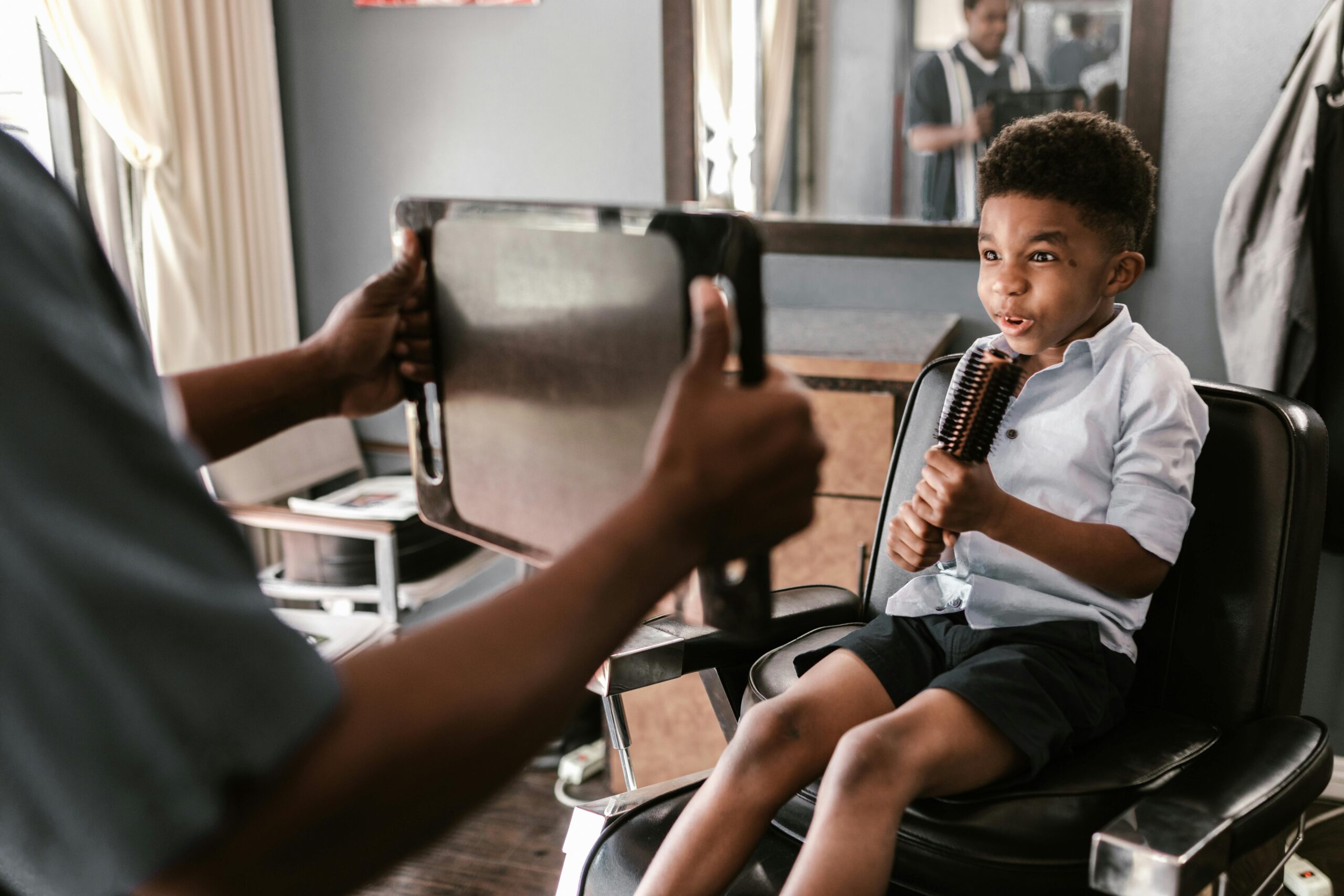 Young child sitting calmly in a barber chair while a stylist shows him his haircut in a mirror, creating a positive and supportive haircut experience for a child with sensory sensitivities.