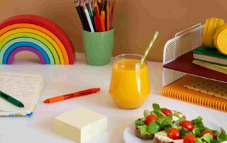 Colorful children's desk with rainbow toy, school supplies, juice, and a healthy snack representing a structured autism school break routine at home