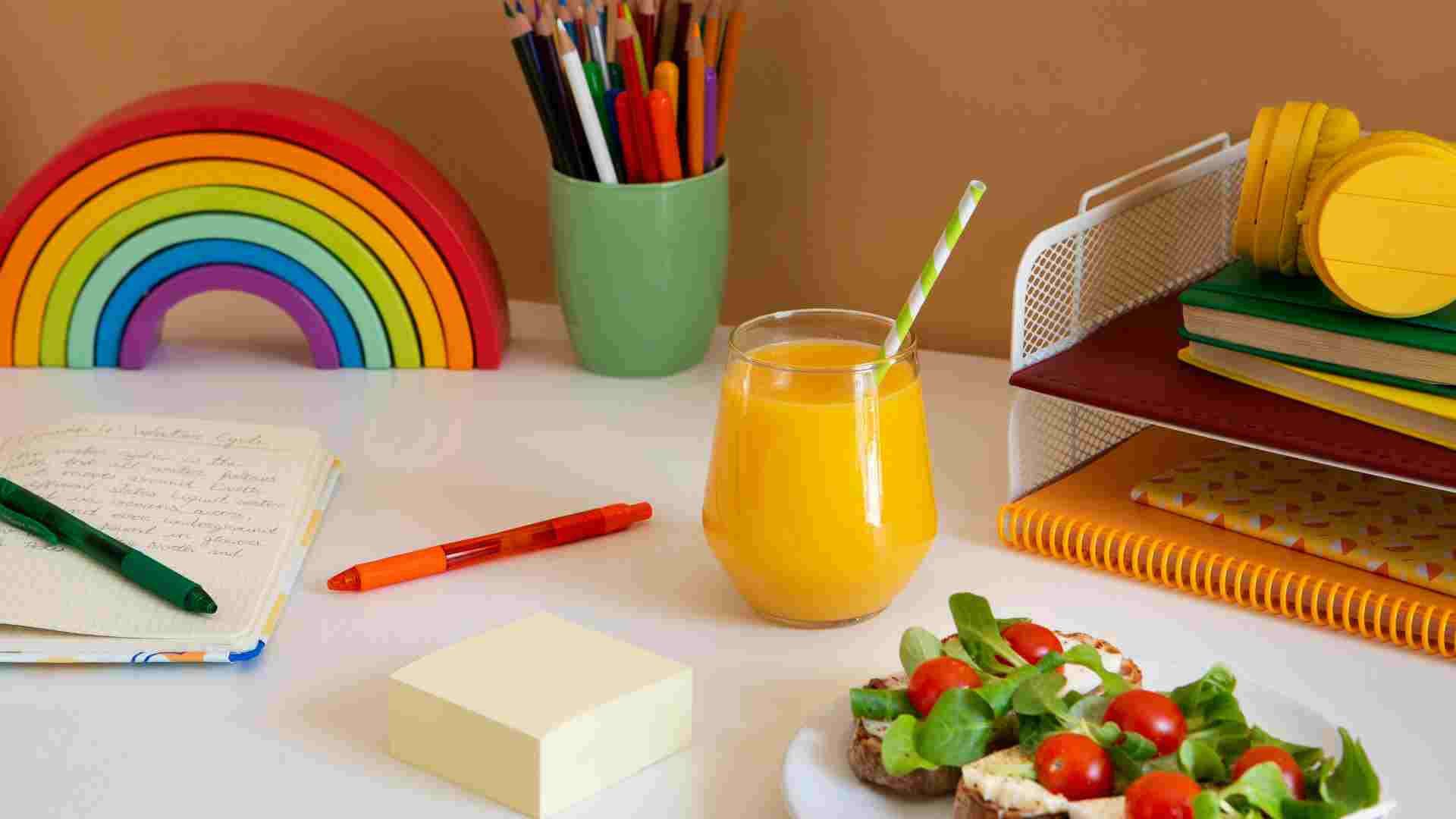 Colorful children's desk with rainbow toy, school supplies, juice, and a healthy snack representing a structured autism school break routine at home