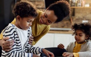Smiling mother helping two young children with autism practice learning activities at home, supporting home school consistency through engaged parent involvement