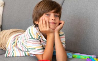 Relaxed young boy with autism lying on a couch during quiet downtime at home, with sensory fidget toys nearby to support regulation and recovery