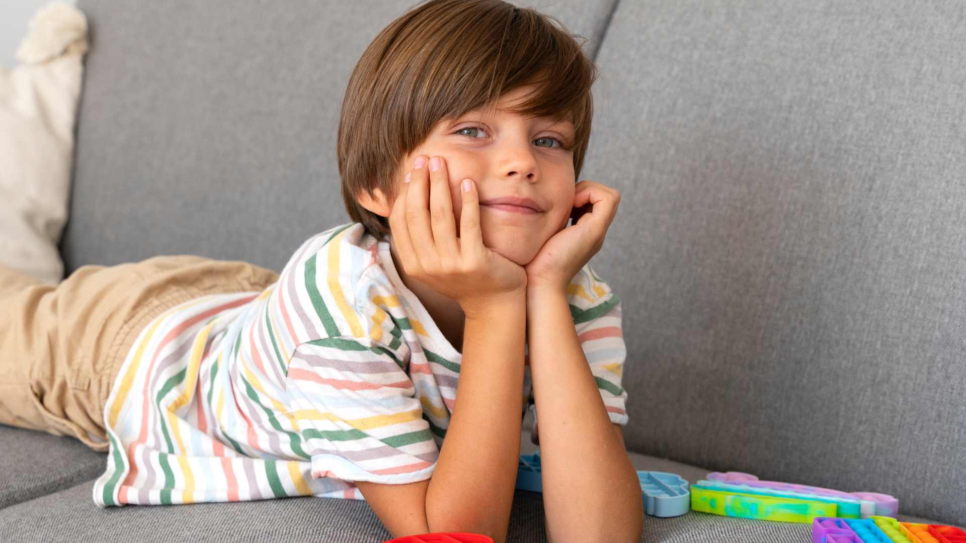 Relaxed young boy with autism lying on a couch during quiet downtime at home, with sensory fidget toys nearby to support regulation and recovery
