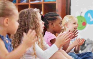 Diverse group of children sitting together in a classroom clapping during a structured group activity, building friendship and social skills