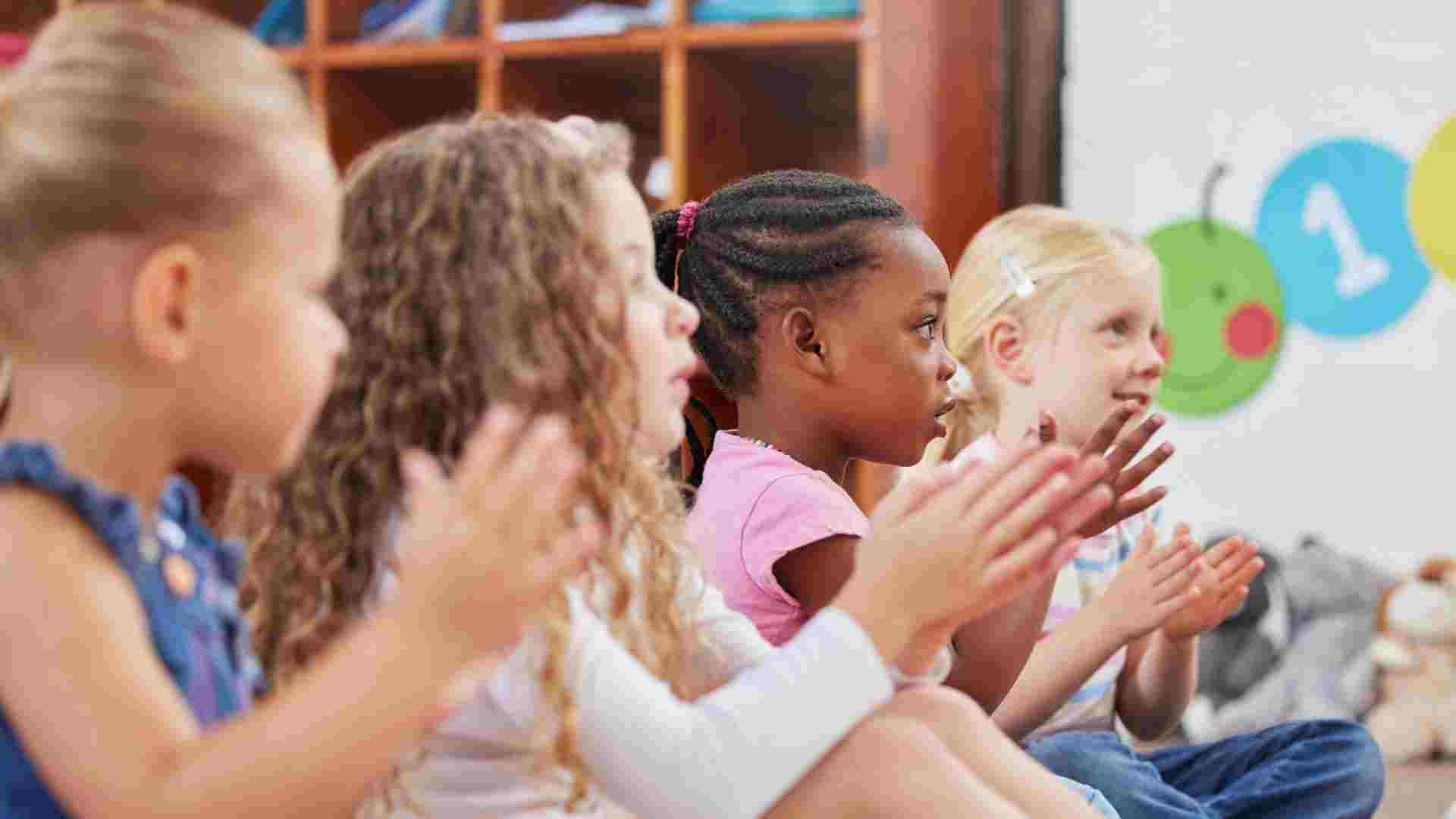 Diverse group of children sitting together in a classroom clapping during a structured group activity, building friendship and social skills