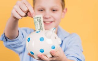 Smiling young boy proudly putting a dollar bill into a spotted piggy bank, practicing the money saving skills children with autism can build through early financial education
