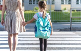 Mother holding her young daughter's hand while crossing a street crosswalk together, practicing community safety skills for children with autism