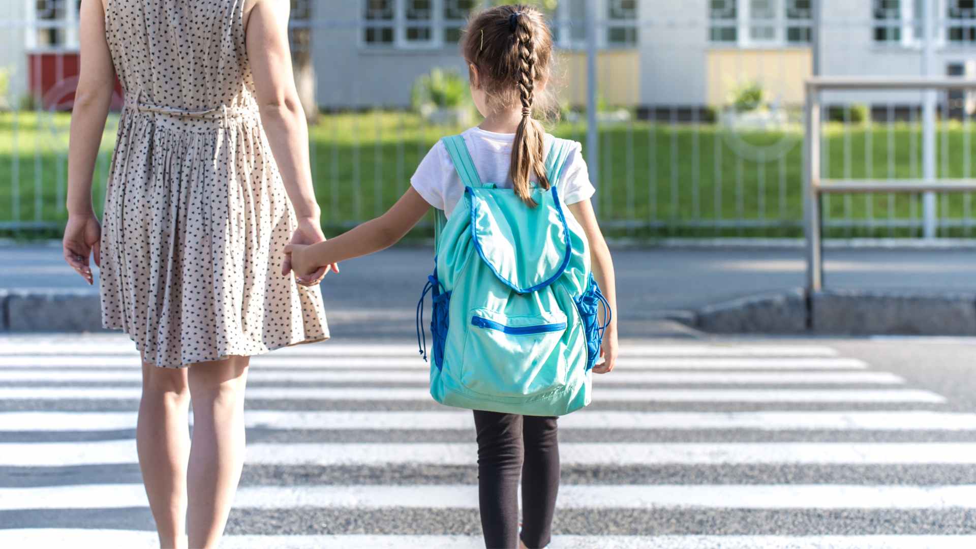 Mother holding her young daughter's hand while crossing a street crosswalk together, practicing community safety skills for children with autism