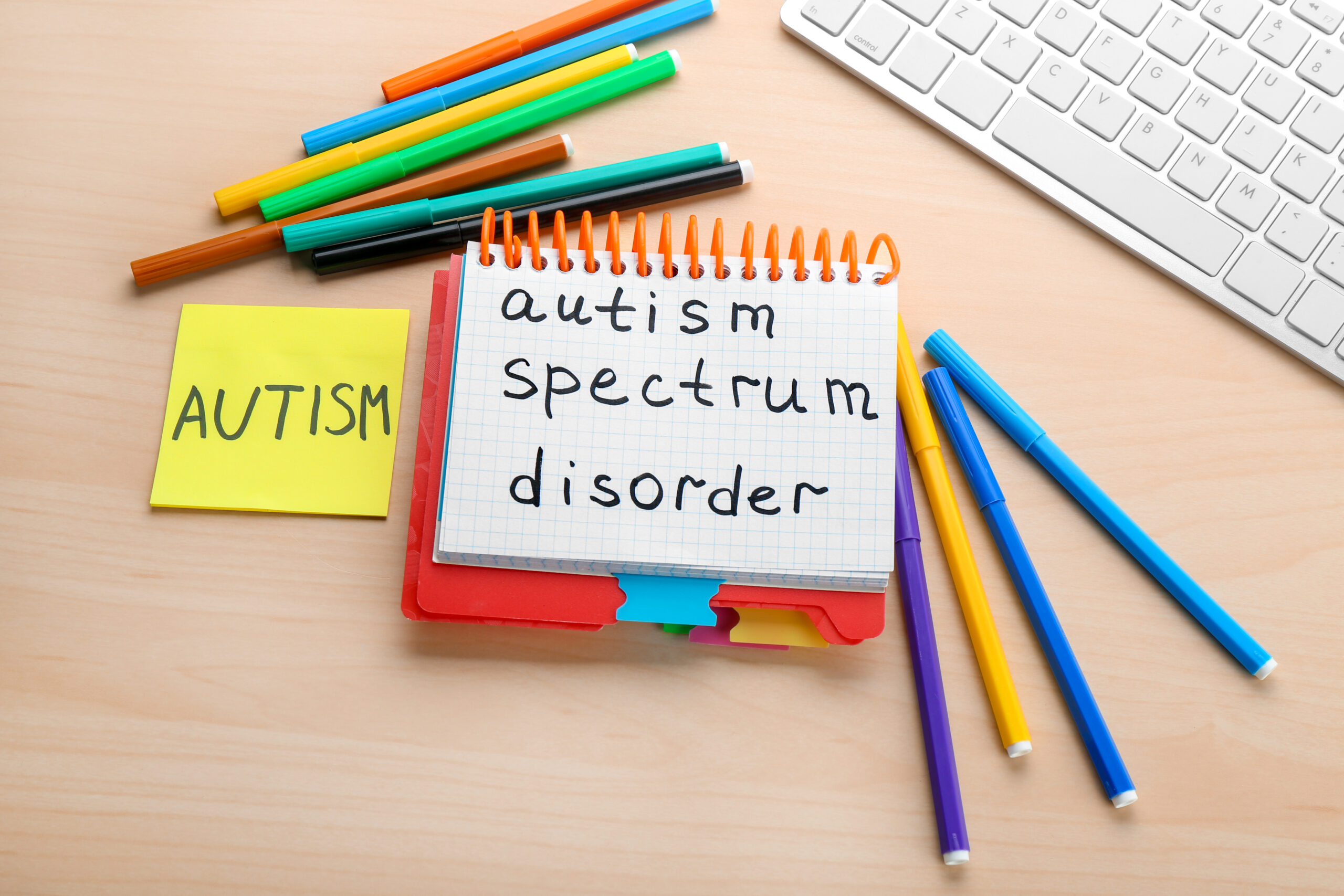 Notebook with autism spectrum disorder written on it alongside colorful markers, representing the autism diagnosis process for Maryland families