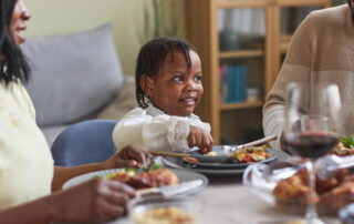 Young child with autism happily participating in a family meal at the dinner table, representing the goal of ABA feeding therapy for food selectivity in Maryland