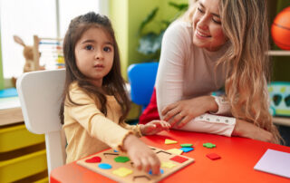 Behavior technician working one-on-one with a young child on a learning activity at a classroom table, illustrating school-based ABA therapy support in Maryland