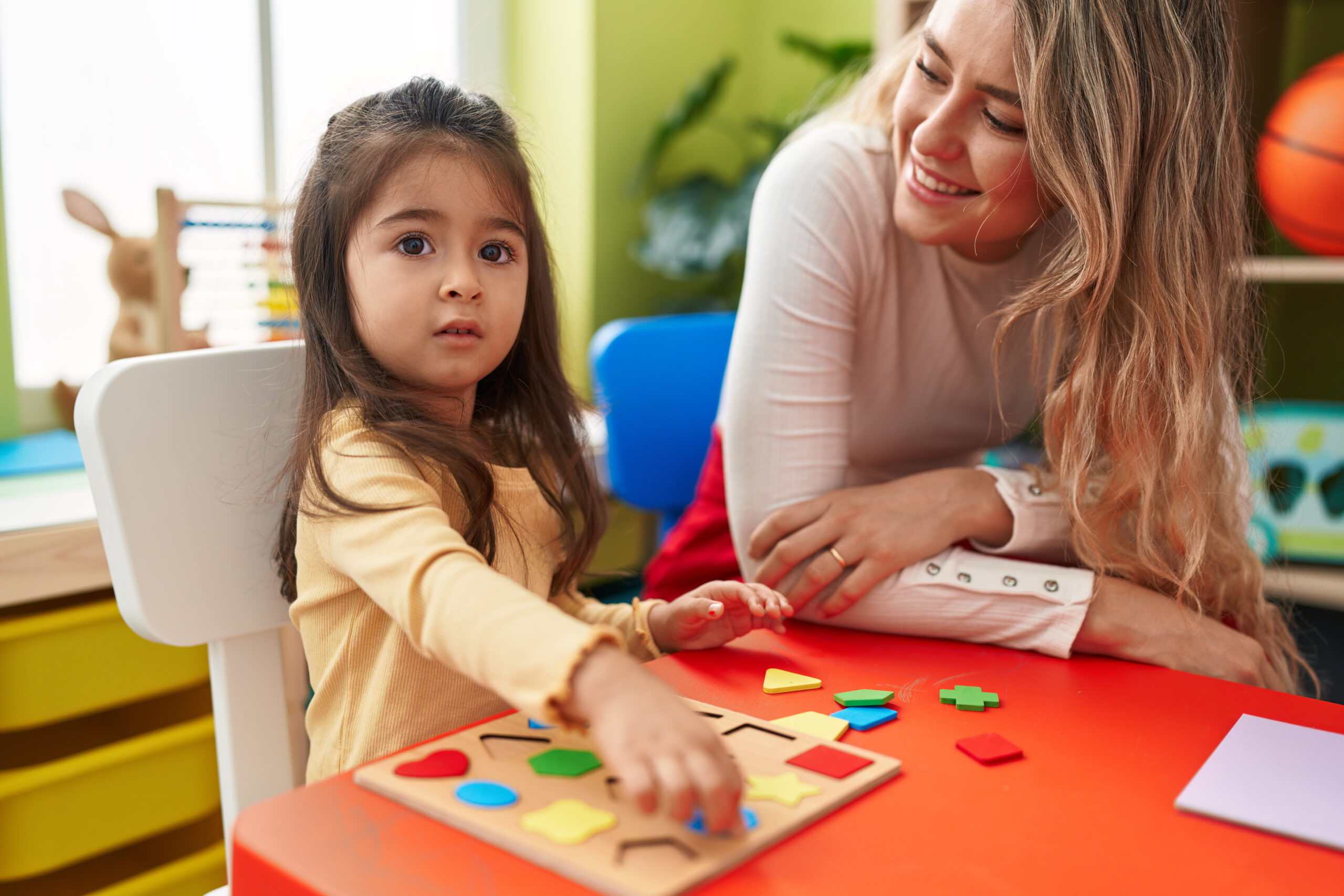 Behavior technician working one-on-one with a young child on a learning activity at a classroom table, illustrating school-based ABA therapy support in Maryland